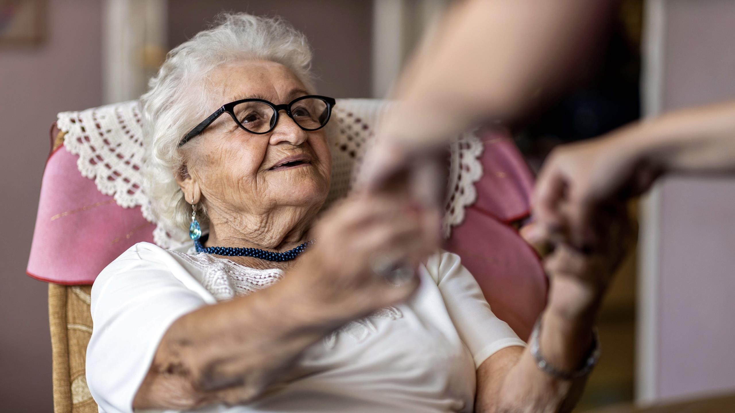 Eldre dame smiler og holder noen i hendene.