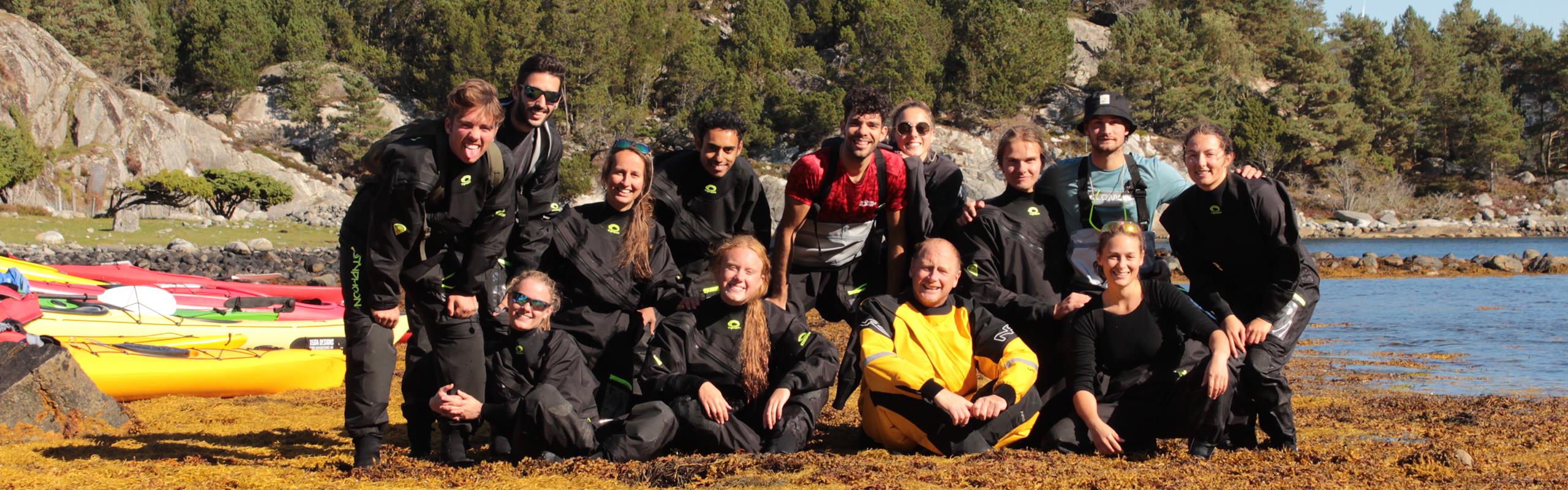 Photo of 13 people in wetsuits on the shore.