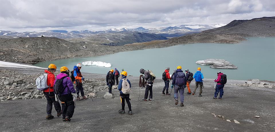 Studenter på tur med hjelmer og sekker ved brevann på høyfjellet. 