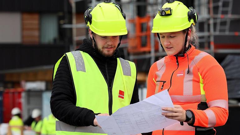 To arbeidstakere på en byggeplass snakker sammen.