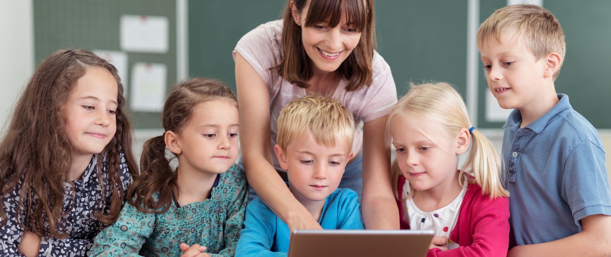 En lærer holder en Ipad og viser noe på den for flere barnehagebarn som sitter rundt. 