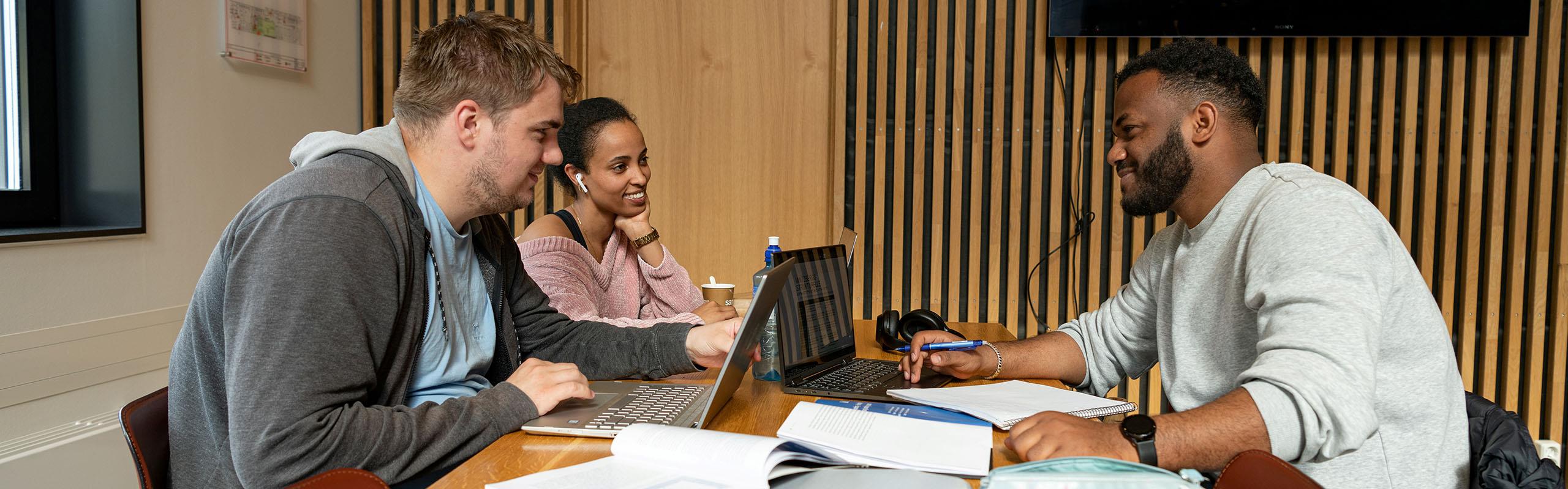 Tre studentar som sit ved bord og jobbar med skulearbeid. 